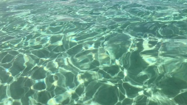 Rippling  of crystal clear translucent water surface with view on white Mediterranean sandy sea floor in 4k