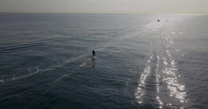 Aerial Following foil surfer going towards the sun over calm and open ocean