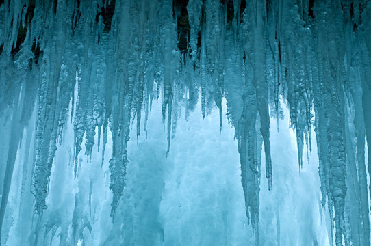 View from behind the frozen curtain of icicles of a frozen waterfall.