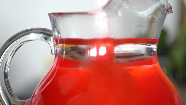 Red powder drink mix pouring into glass pitcher of water.