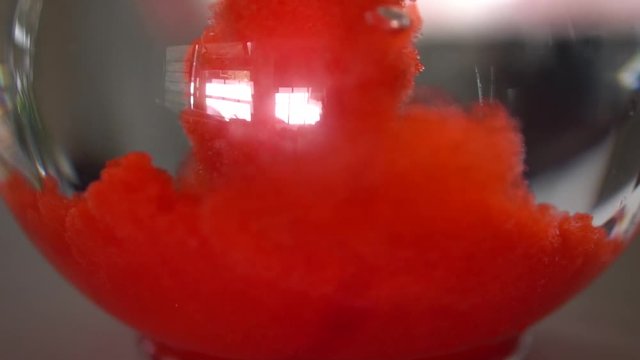 Red powder drink mix pouring into bottom of glass pitcher or water. Slow-mo
