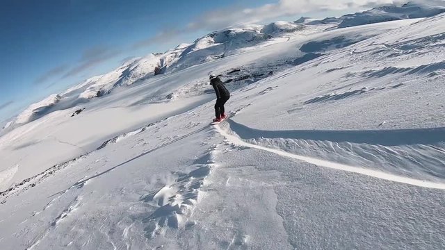FOLLOW: girl snowboarding epic backcountry mountain range. Woman freeriding in fresh powder downhill on sunny day.