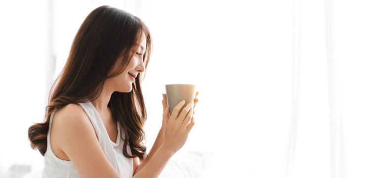 Portrait of smiling happy cheerful beautiful pretty asian woman relaxing drinking and looking at cup of hot coffee or tea.Girl felling enjoy having breakfast in holiday morning vacation on bed at home