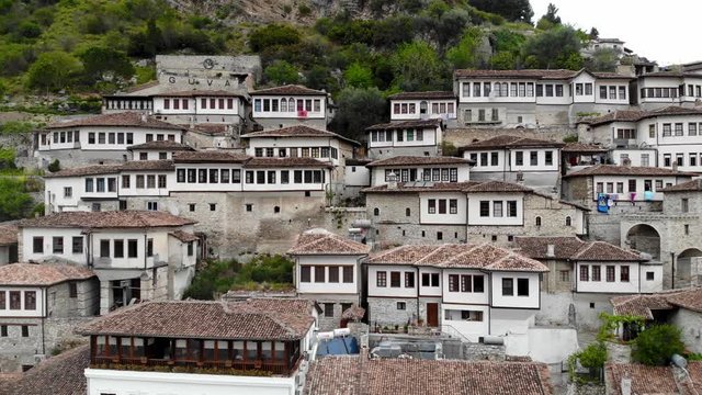 White houses with big windows over stone walls on slope of rocky mountain in Berat, Albania, pan shot