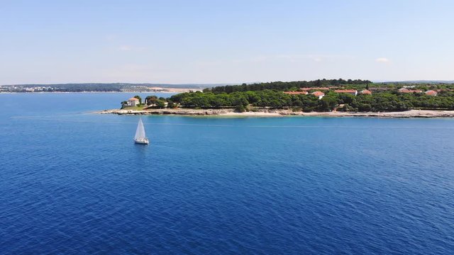 Aerial: Lonely sailing boat cruising near the shore into the open sea.