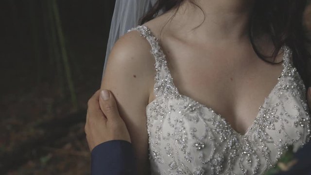 Close-up shot of a brides ivory wedding gown bodice with groom caressing brides arm