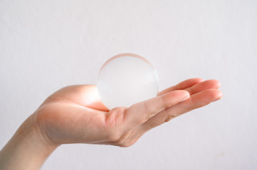 Fototapeta na wymiar Close up of someone hand holding a clear transparent Crystal ball. The use of crystal balls to predict the future is viewed as pseudoscience.