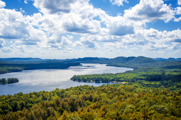Fulton Chain Lakes view from the Adirondack Mountains in Upstate New York. Taken from the mountain summit after a short hiking trail. Lots of trees and clouds over the water. Camping in the Catskills