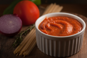 tomato sauce on a bolw over a wood table with spaghetti tomato purple onion and rosemary 