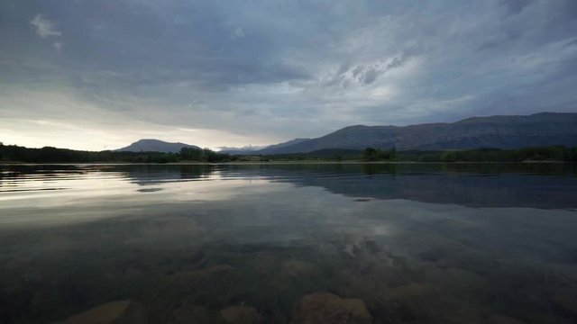 Small gentle ripples on the rocky shores of Peruća Lake, high dark storm clouds reflecting the horizon, Croatia