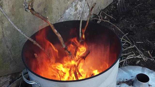 Slow motion shot looking into a metal drum with garden waste burning.