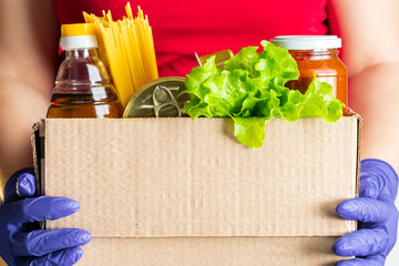 A woman volunteer is holding a donation box with foodstuffs. Delivery of necessary food during an...