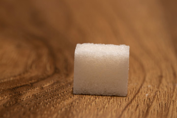 Photo of a single sugar cube on a wooden brown surface.
