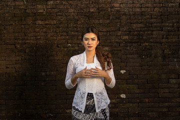 Portrait of beautiful south east asian woman wearing jewelry and white traditional cloth with brick wall background.Calm face expression medium close up photography.