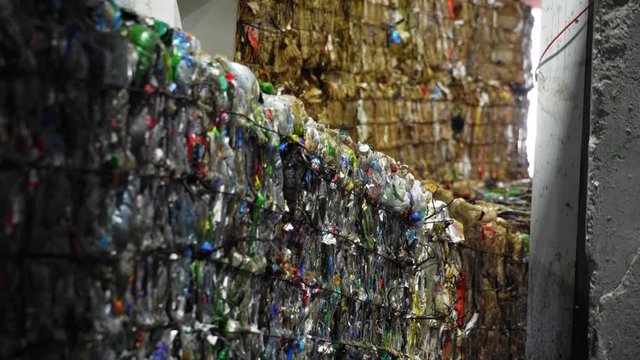 RUSSIA, TVER - JUNE 20, 2019: BRIQUETTES of COMPRESSED PLASTIC WASTE lined up on a CONVEYOR inside an INDUSTRIAL RECYCLING PLANT. Shot at a WASTE SORTING FACILITY with muted lighting.