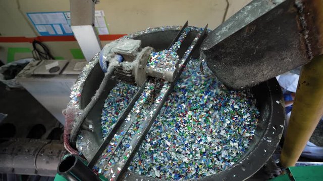 Colorful PET FLAKES move along a conveyor belt and fall into a melting machine inside a RECYCLING PLANT. A glimpse into plastic processing and environmental reuse.