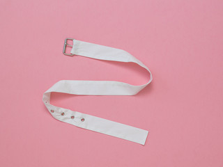 White cloth belt with metal buckle on pink background. The concept of differentiation.