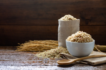 Cook and raw brown rice in white ceramic bowl on wood table and wood background with spoon. Copy space.