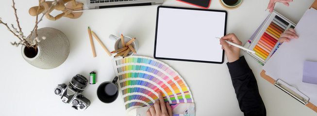 Overhead shot of designer working on mock-up digital tablet, designer supplies and decorations