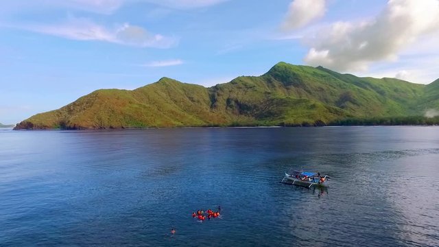Aerial View of People Swimming in the calm sea beside a small boat with a background of green island - Nagsasa Cove, Zambales, Philippines.