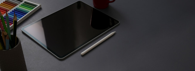 Cropped shot of dark concept office desk with digital tablet, stylus pen, designer supplies and copy space