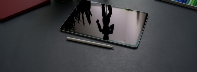 Cropped shot of dark concept office desk with digital tablet, stylus pen and office supplies