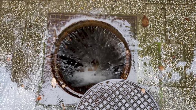 Stream of water flowing down an open sewer grate, after heavy rain that flooded the path.