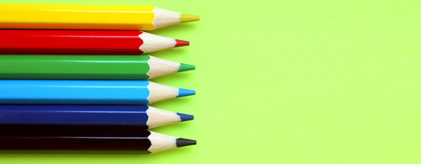 Colored pencils on a yellow background. 6 colors Black, blue, blue, green, red, yellow. Pencils are well-honed. Flatlay. Isolated. Art. Art therapy. Leisure. Pencils are placed on the left. Banner