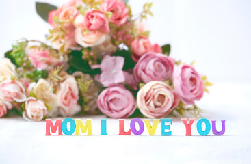 Obraz na płótnie Canvas Mom, i love you - text of colorful letters and flowers on light background. Mothers Day holiday concept