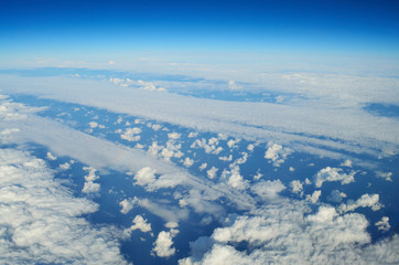 Fototapeta premium Top view from the plane window. White, small Cumulus clouds alternate with solid ones against a blue sky.