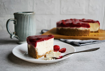 Piece of cheesecake with strawberry jelly on a white plate. The background is light, side view, horizontal orientation.