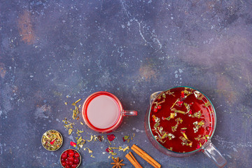 Red tea (rooibos, hibiscus, karkade) in glass cup and teapot among cinnamon, anise, cranberries on a dark background. Herbal, vitamin, detox tea for cold and flu. Close up, copy space for text