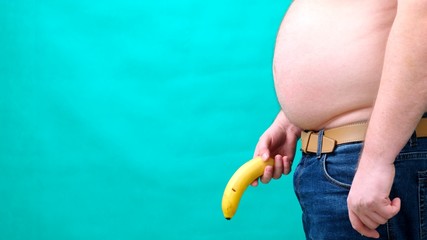 A man with a large belly holds a banana lowered to the bottom of. male sexuality, man sex and...