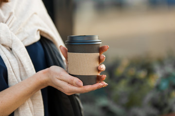 beautiful woman's hands with cup of coffeen in craft paper in the street