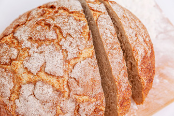 A sliced head of leavened self-made brown bread covered in flour on a table.