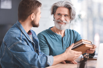 Mentor giving books to young photographer in studio