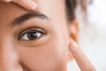 Young African-American woman putting in contact lenses, closeup