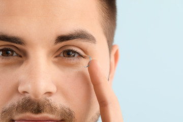 Young man with contact lens on color background, closeup
