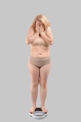 Obraz premium Sad overweight woman with scales on grey background. Weight loss concept