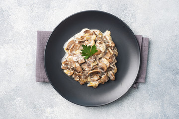 Stewed mushrooms champignons in sauce with sour cream and cheese parsley on a plate. Copy space.