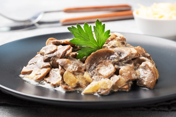 Stewed mushrooms champignons in sauce with sour cream and cheese parsley on a plate.