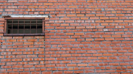 red brick wall with a small window covered with rusty metal bars