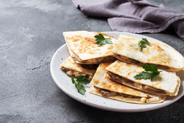 Pieces of quesadilla with mushrooms sour cream and cheese on a plate with parsley leaves. Concrete background copy space.