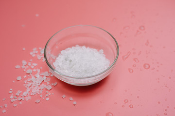 sea salt in a glass bowl on a pink pastel background next to sea water