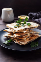 Pieces of quesadilla with mushrooms sour cream and cheese on a plate with parsley leaves. Wooden background close up.
