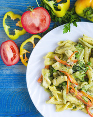 Pasta with vegetables and cheese in a white plate on a blue wooden background vertical