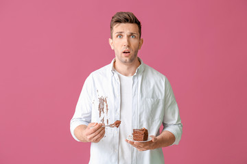 Troubled man in dirty clothes eating chocolate cake on color background