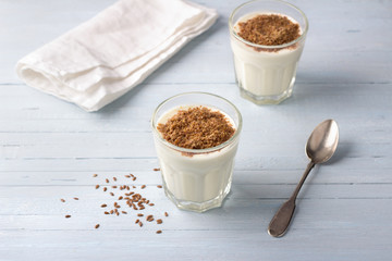 Simple healthy breakfast or snack. Natural yogurt with ground flax seeds in glasses on a light blue background