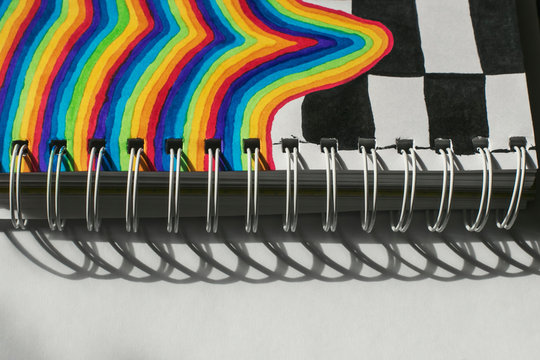 Children's drawing with markers in a sketchbook with springs: a bright fantasy rainbow with a chessboard. Illustration of joy and good mood. Black and white drawings.
