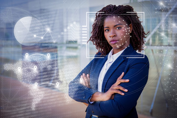 Woman posing near building and virtual identification graphics. Young African American businesswoman with arms crossed standing outside, looking at camera. Confident businesswoman concept